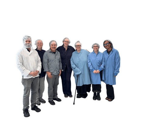 Group of seven people wearing hairnets and protective coats, standing together and smiling, likely in a food processing or facility setting.