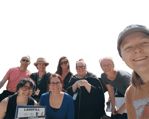 Group of people smiling together outdoors, holding a landfill sign, suggesting a team visit or educational activity related to waste management.
