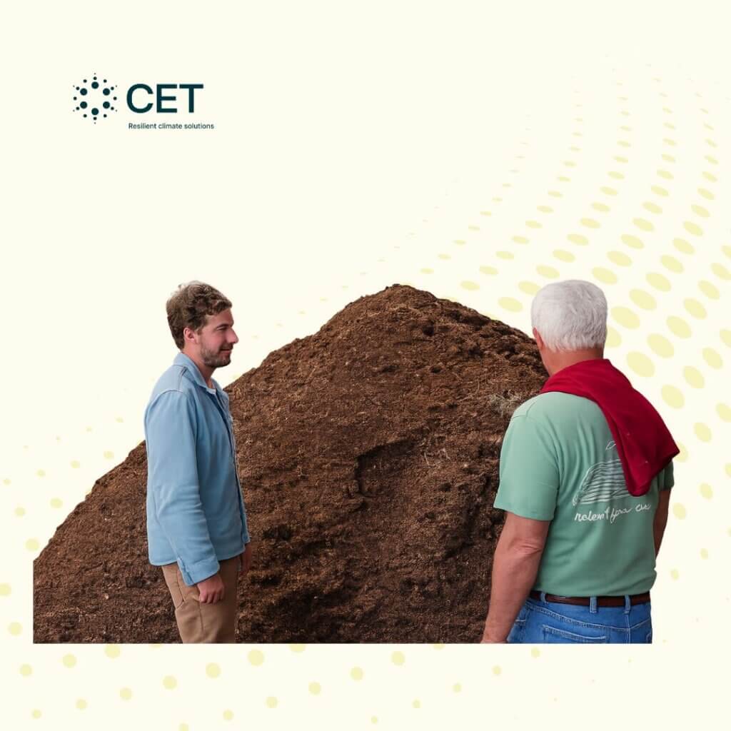 compost farm (2) Two people standing beside a large pile of compost inside a farm facility, discussing composting operations.